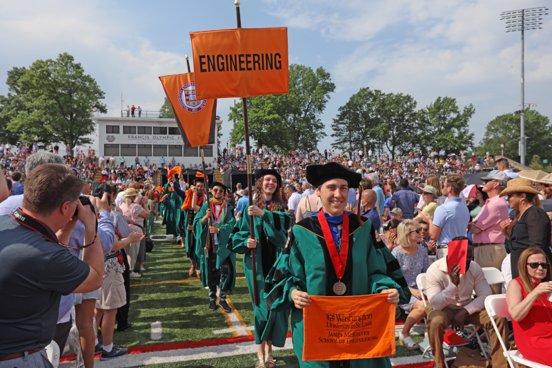 Graduate marshals carry their orange school flag into the ceremony.